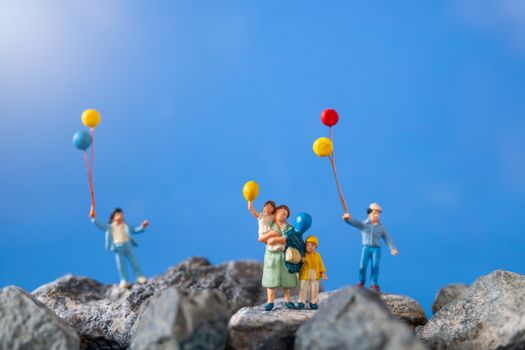 Miniature people , Happy family holding balloon on The rock with blue sky background