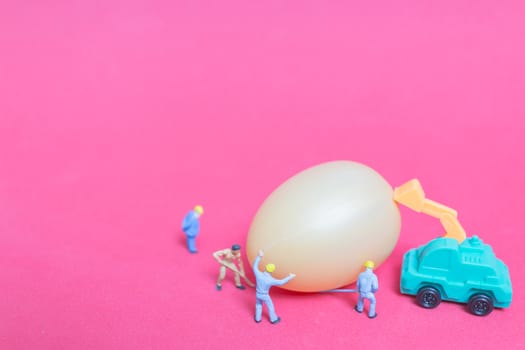 Miniature people work at Easter-eggs for Easter day on pink background