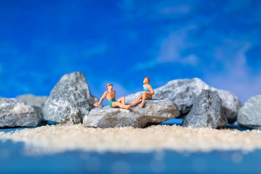 Miniature people wearing swimsuit relaxing on the beach with blue background , Summer time concept
