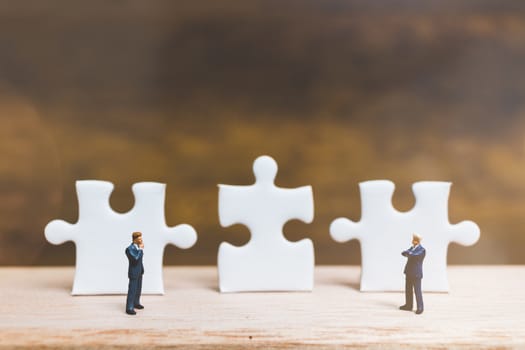 Miniature people: Businessman standing on jigsaw with wooden background : Business concept.