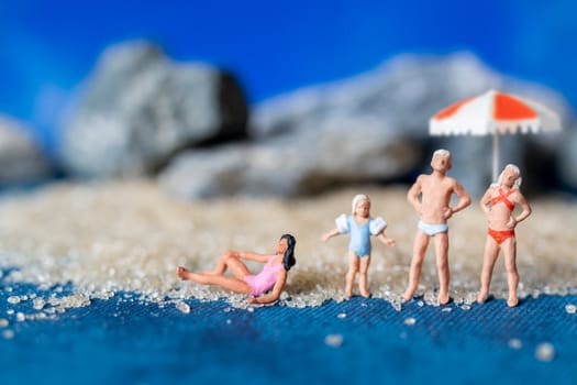 Miniature people wearing swimsuit relaxing on the beach with blue background , Summer time concept