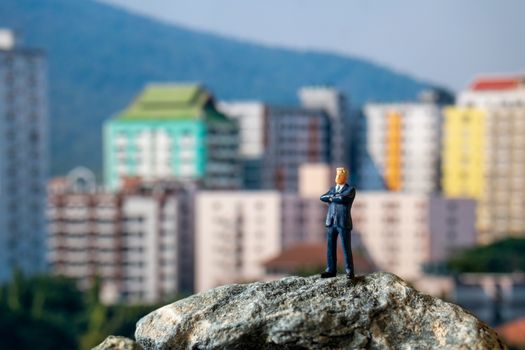 Miniature people , Businessman standing on The rock with building background
