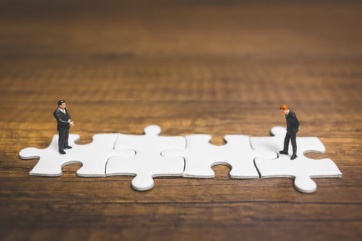 Miniature people: Businessman standing on jigsaw with wooden background : Business concept.