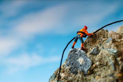 Miniature people: Hikers climbing up on the rock . Sport and leisure concept.