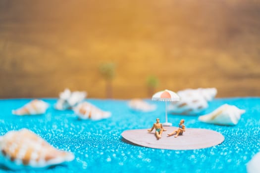 Miniature people wearing swimsuit relaxing on a seashell with blue glitter background