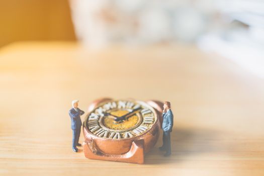 Miniature people: Businessman standing with Ancient clock on wooden background