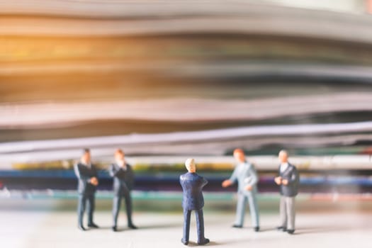 Miniature people: Businessman standing and stack of book with warm lighting background