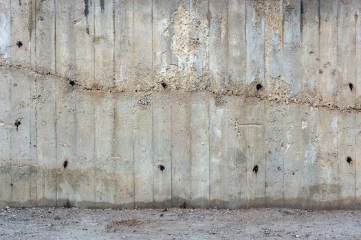 an outdoor thick rough gray concrete wall with part of floor surface, visible imprints of wooden planks, twice filled