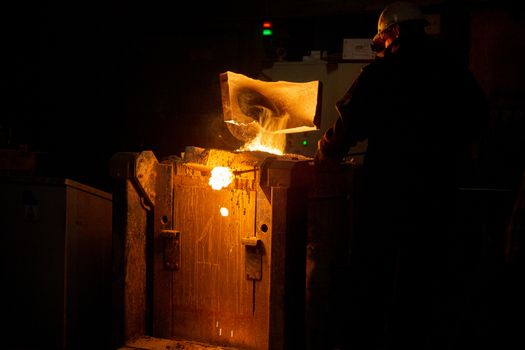 Worker removing slag from metallurgical furnace with exhaust hood and melting metal with vapor. Selective focus technique.