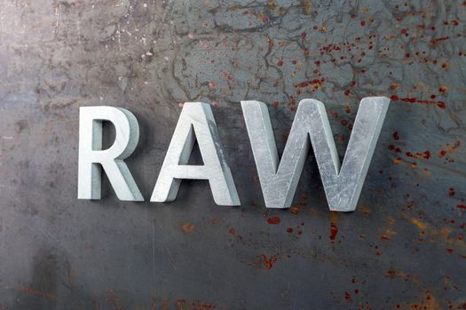 the word raw laid with silver metal letters on hot rolled steel sheet surface - close-up with selective focus and skewed perspective
