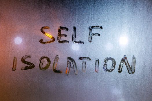 the words self isolation handwritten on wet window glass at night - close-up fuul frame picture with selective focus and background blur