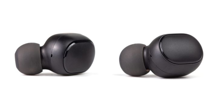 two black wireless bluetooth earbuds isolated on white background - close-up with selective focus.