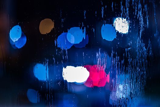 red and blue night police lights bokeh trough wet glass close-up with selective focus abstract background