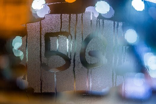 the word 5G handwritten on night wet window glass with selective focus and bokeh blur background.