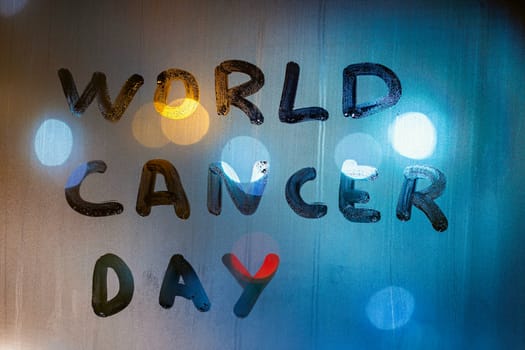 the words world cancer day handwritten on night window foggy glass - close-up with background blur