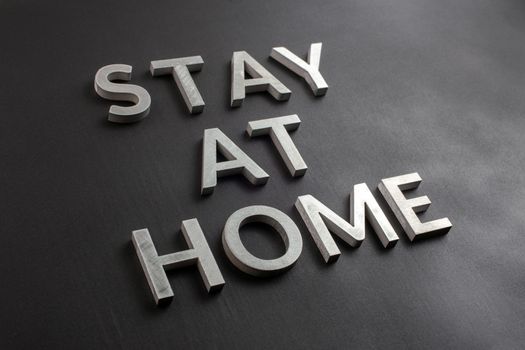 the words stay at home laid with silver metal letters on matte black background in diagonal perspective, slanted full frame view