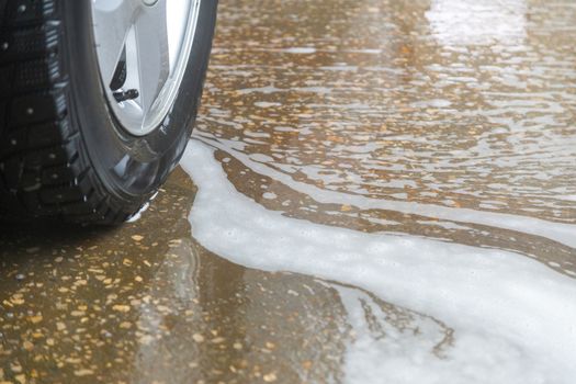 A close-up view of civil car wheel in soap puddle on the floor of washing garage. Car wash and environmental conservation concept picture.