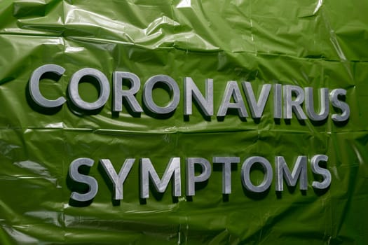 the words coronavirus symptoms laid with silver letters on crumpled green plastic film - linear perspective composition with selective focus and dramatic light