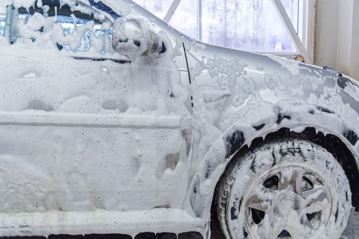 a side view of car covered by soap foam while washing indoors - close-up with selective focus.