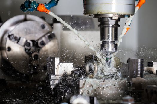 A process of vertical cnc steel milling with external water coolant streams, splashes and a lot of metal chips. Fast shutter speed for motion freezing.