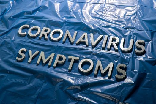 the words coronavirus symptoms laid with silver letters on crumpled blue plastic film - diagonal perspective composition with dramatic light