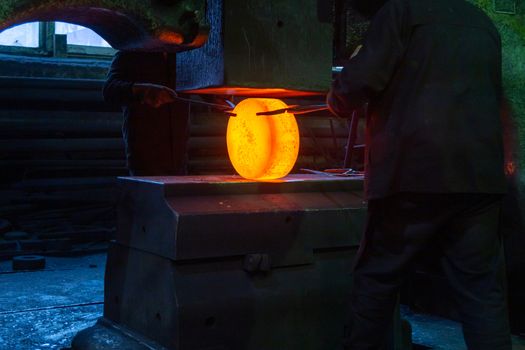 close-up picture of hot steel manual forging process with big mechanical hammer machine, sparks flying out from workpiece