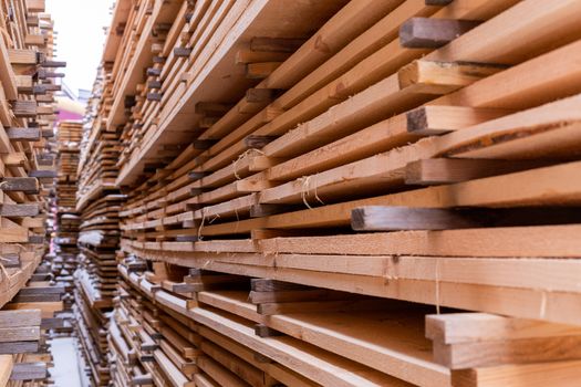 Large stacks of wooden planks background with selective focus and linear perspective. Winter woodwork industrial storage.