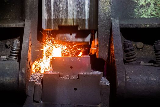 close-up frontal view of hot steel forging process with big mechanical hammer machine, sparks flying out from workpiece