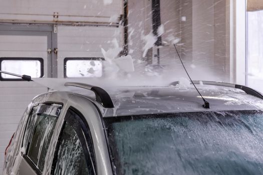 Indoor self car washing. Process of removing soap foam from roof of vehicle with high pressure water stream - close-up vith selective focus and motion blur.