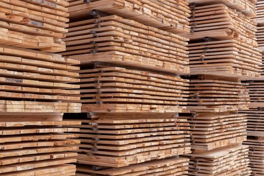 Large stacks of wooden planks full frame background with selective focus and linear perspective. Woodwork industrial storage.