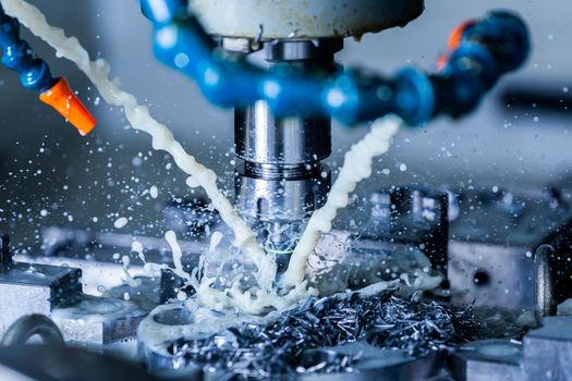 A process of vertical cnc steel milling with external water coolant streams, splashes and a lot of metal chips. Fast shutter speed for motion freezing, close-up with selective focus, shallow depth of field and background blur.