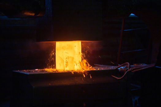 close-up picture of hot steel manual forging process with big mechanical hammer machine, sparks flying out from workpiece