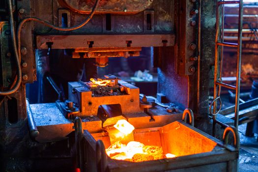 Close-up picture of fresh forged hot steel workpieces after press forming in dirty dark factory. Selective focus on foreground.