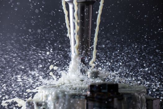 Abstract process of vertical cnc steel milling with external water coolant streams and splashes, close-up with selective focus and background blur. Fast shutter speed for motion freezing.