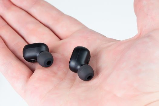 a pair of black wireless bluetooth earbuds laying on caucasian palm - close-up with selective focus