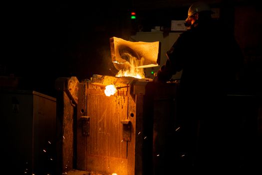 Worker removing slag from metallurgical furnace with exhaust hood and melting metal with vapor. Selective focus technique.