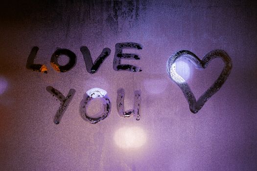 the words love you handwritten on foggy night window glass and heart symbol at the right side