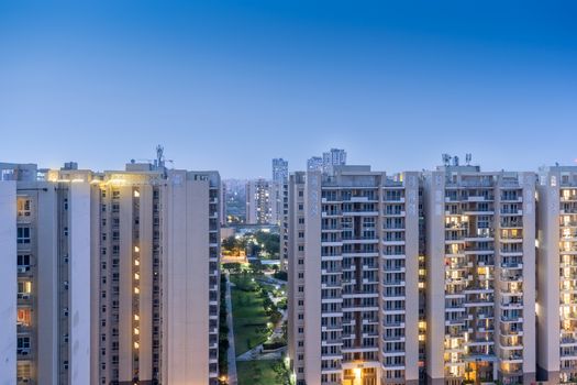 Aerial dusk shot of buuldings with warm orange lights shining out of the newly constructed homes offices and residences . Shows the elegance and opulence of the real estate sector in cities like Gurgaon, Mumbai, Jaipur, bangalore, mumbai and more