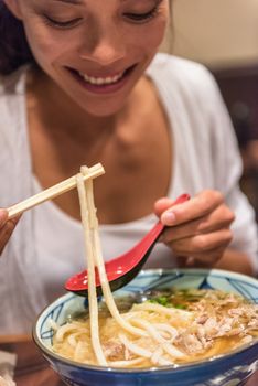 Ramen noodles girl eating soup bowl at japanesese restaurant at night. City travel lifestyle.