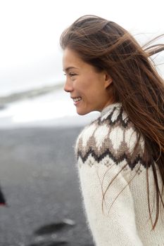 Winter iceland sweater Asian woman model wearing traditional wool knit icelandic clothing wear. Pretty multiracial girl walking on black sand beach looking pensive smiling happy.