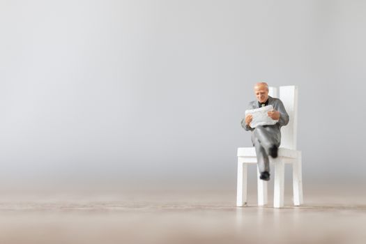 Miniature people: Businessman reading book on  chair , Education or business concept.
