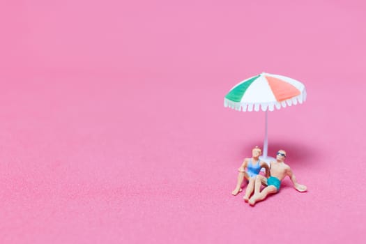 Miniature people wearing swimsuit relaxing on pink background , Valentine's day concept