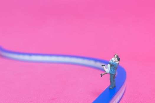 Miniature people : Couple hugging on The bridge on pink background , Valentine's day concept