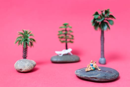 Miniature people wearing swimsuit relaxing on the rock with pink background , Valentine's day concept