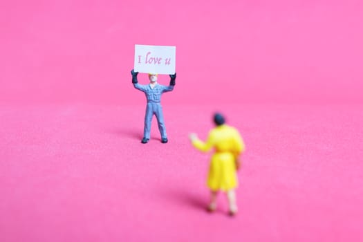 Miniature people: Holding paper board "I love you " on pink background , Valentine's day concept
