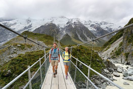 Tourists walking crossing bridge on the Hooker Valley Track hiking trail, New Zealand. Hikers people at Aoraki, Mt Cook National Park with snow capped mountains landscape.