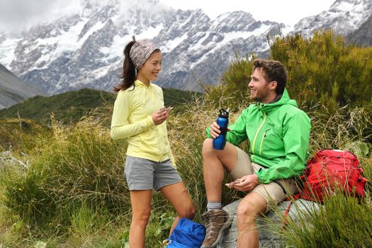 Camping lifestyle young people eating lunch outdoors hiking on New Zealand mountain trail track. Couple trampers tramping in nature with backpacks.