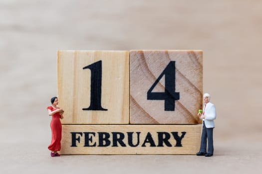 Miniature people couple with wooden block 14 FEB on wooden background, happy valentines day concept