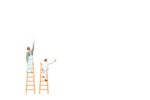 Miniature people with ladder holding brush in front of a white wall background