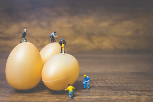 Miniature people work at Easter-eggs for Easter day on wooden background